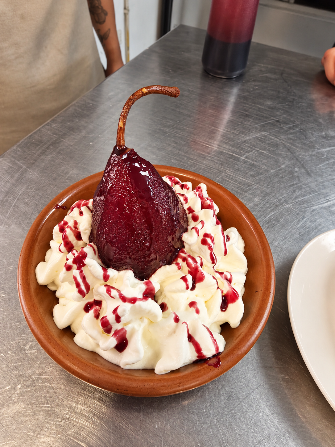 Wine-poached pear with cream, served on a ceramic dish.